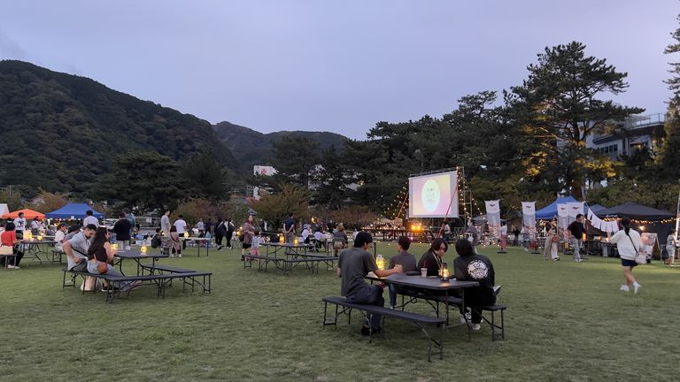 日が沈んだ松原公園で、キャンドルの灯るテーブルに集まり点灯したスクリーンを待つ来場者たち
