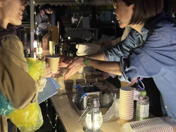 夜、提灯を吊るしたカウンターで飲み物を手にする来場者