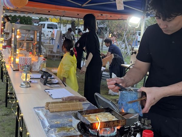 夕方の屋台で、提灯の下に立ち鉄板で調理する出店者