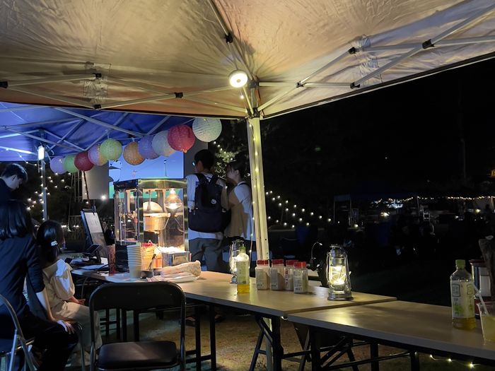 2025年の夜の会場。テントの下にランタンと提灯が灯り、ポップコーンの屋台に人が集まっている